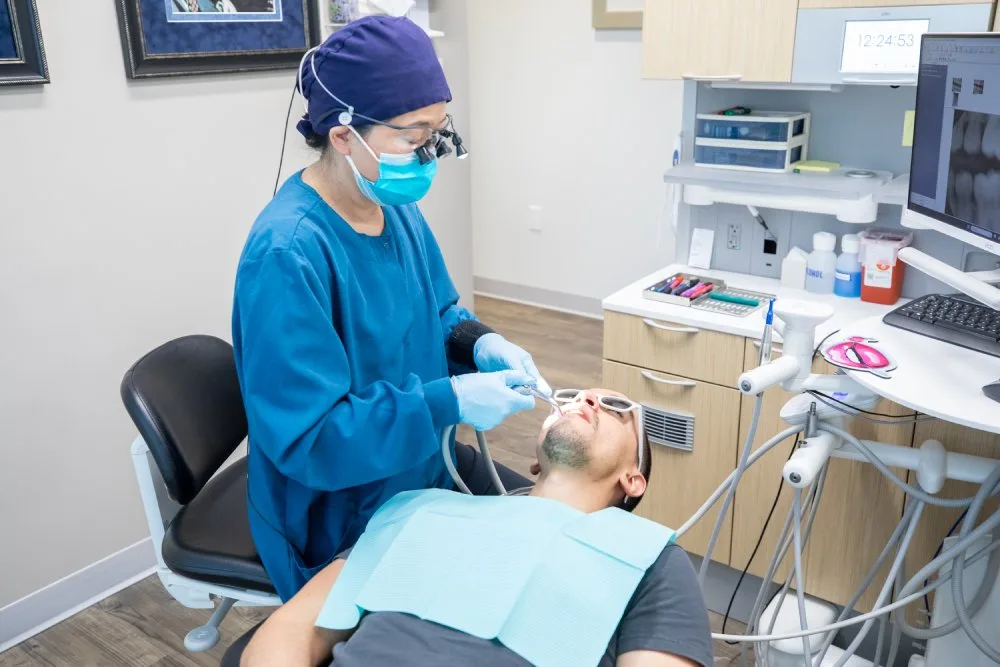 Patient Receiving Dental Cleaning from Hygienist – Kirkland Dental Dental hygienist in protective gear performing teeth cleaning on a patient in a modern dental office – Kirkland Dental