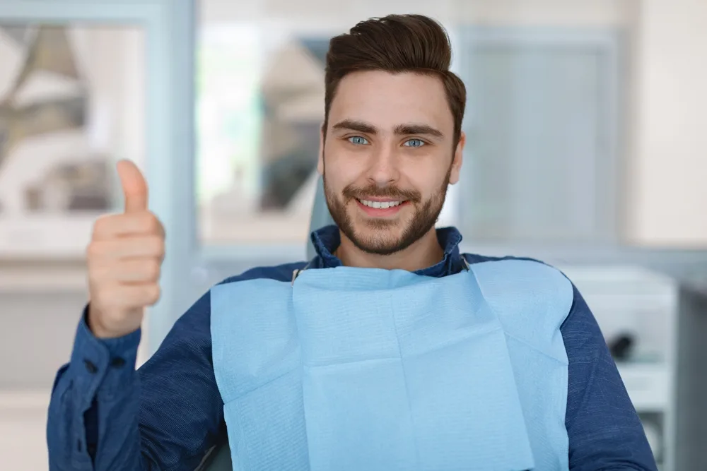 Confident Patient Smiling After Procedure – Dental Implants Kirkland Young man in dental chair giving thumbs up and smiling confidently after implant consultation – Dental Implants Kirkland