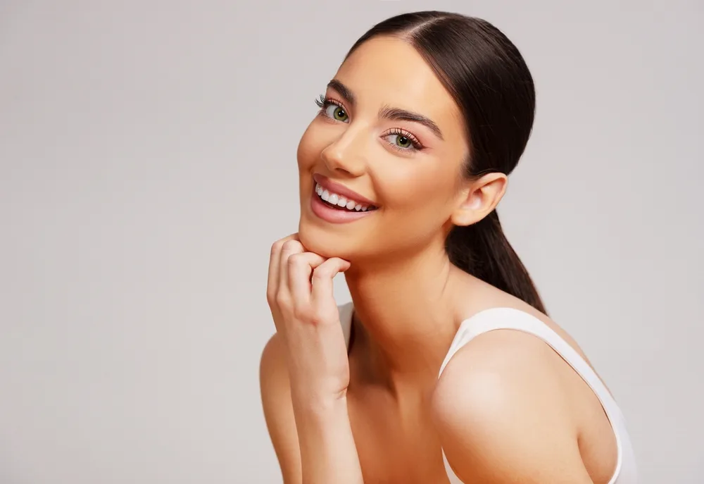 Smiling woman with dark hair pulled back, gently resting her hand beneath her chin.