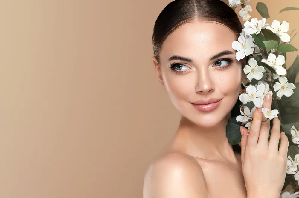Woman Posing Beside White Flowers Woman with dark hair gently touching white flowers beside her face while looking to the side.