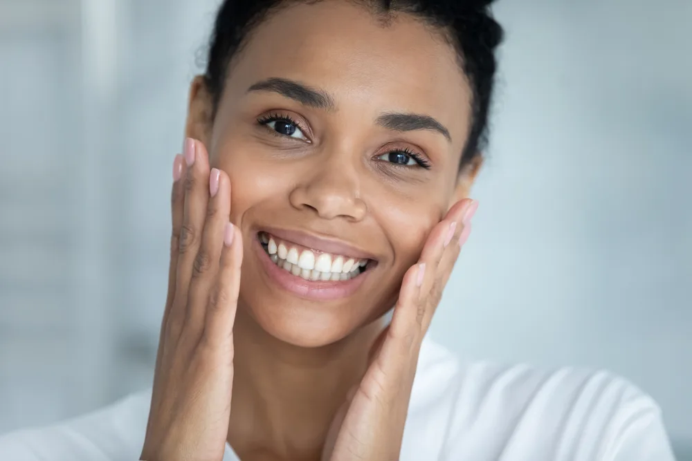 Smiling Woman Gently Touching Her Cheeks Smiling woman with dark hair gently placing both hands against her cheeks.