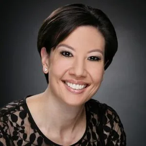 Smiling female dental professional with short dark hair wearing a black lace-patterned top.
