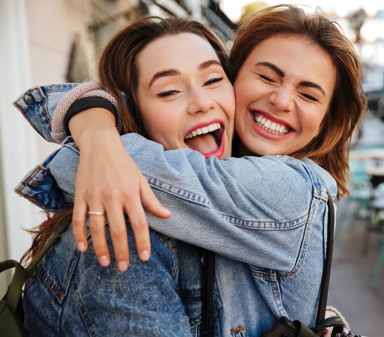 Confident Smiles and Happy Moments – Cosmetic Dentist Kirkland Two young women smiling brightly and hugging outdoors, showing off their beautiful teeth after cosmetic dental care – Cosmetic Dentist Kirkland