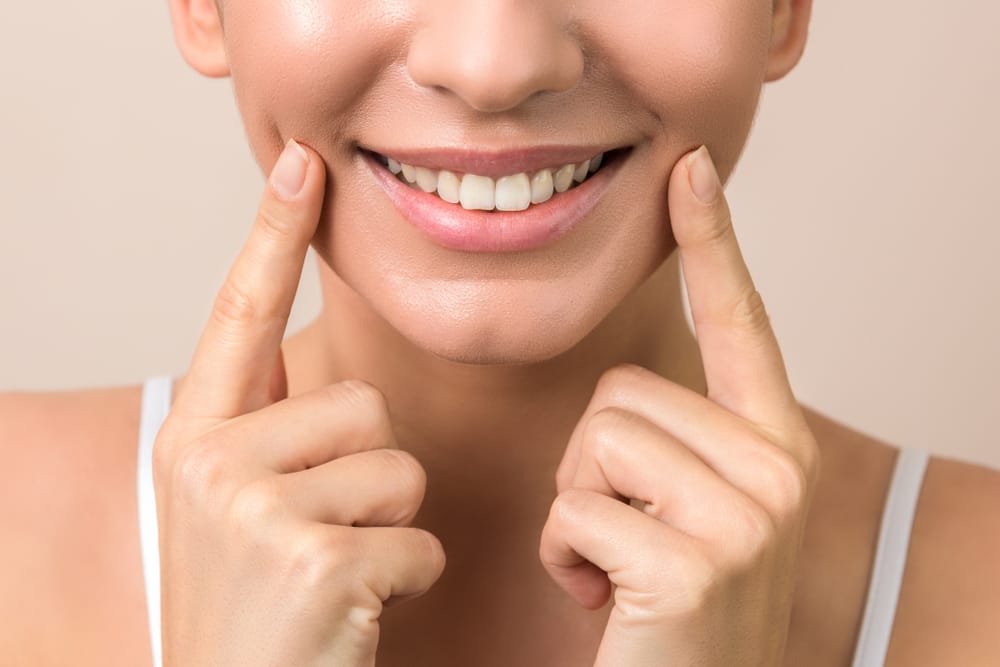 Woman showing smooth skin and radiant smile – Botox Kirkland Close-up of woman pointing to her smooth cheeks and smile after - Botox Kirkland